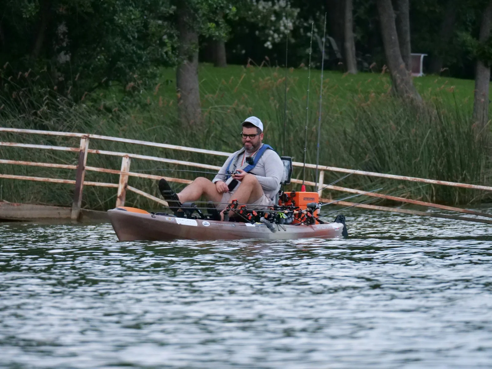 An angler fishing from a kayak beside a wooded lakeshore