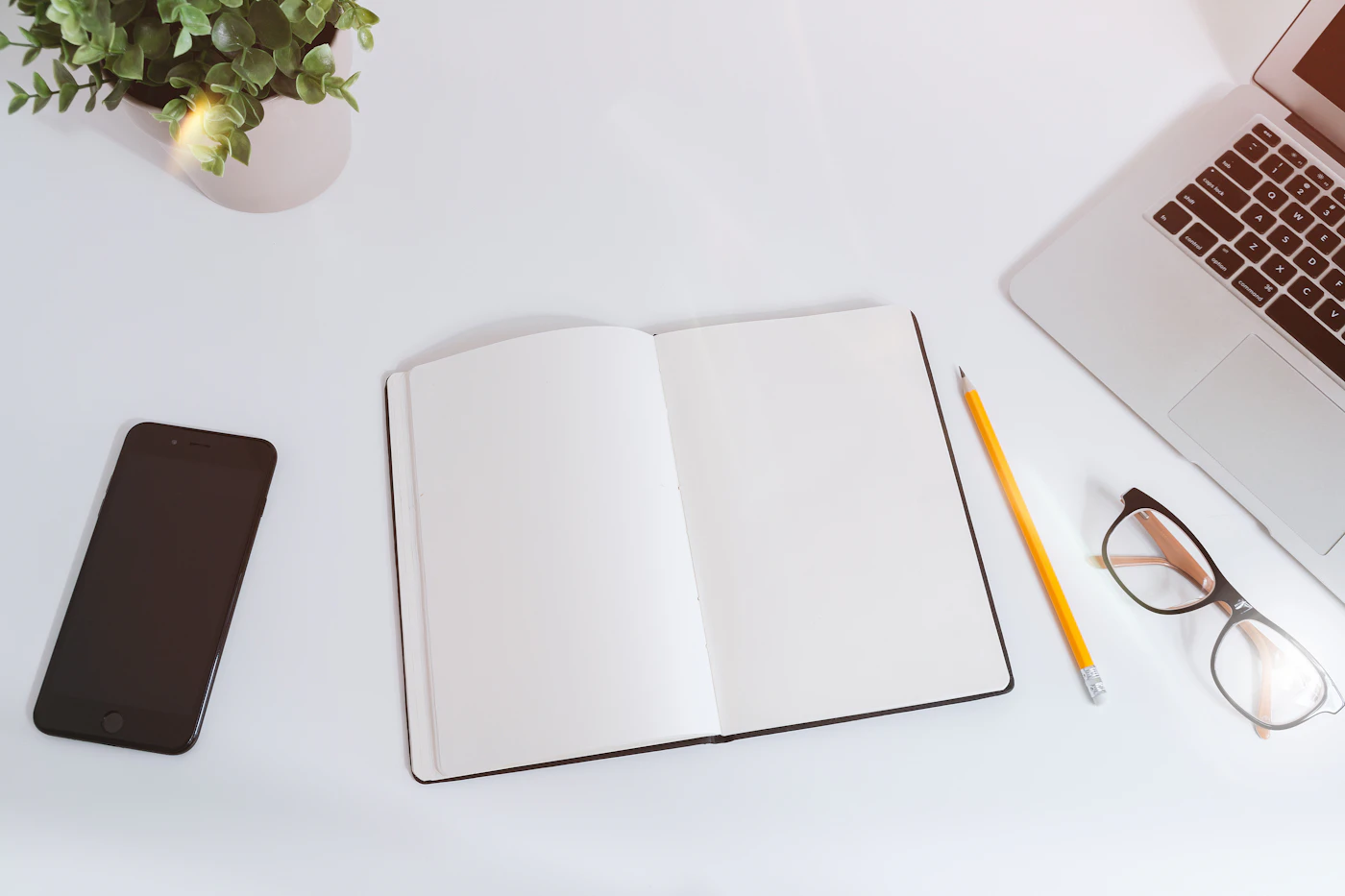 An open notebook beside a laptop and phone on a white desk