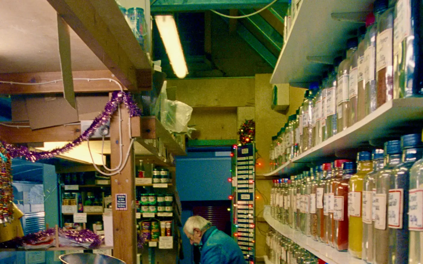 A shopkeeper working in a narrow shop lined with shelves of glass jars and bottles