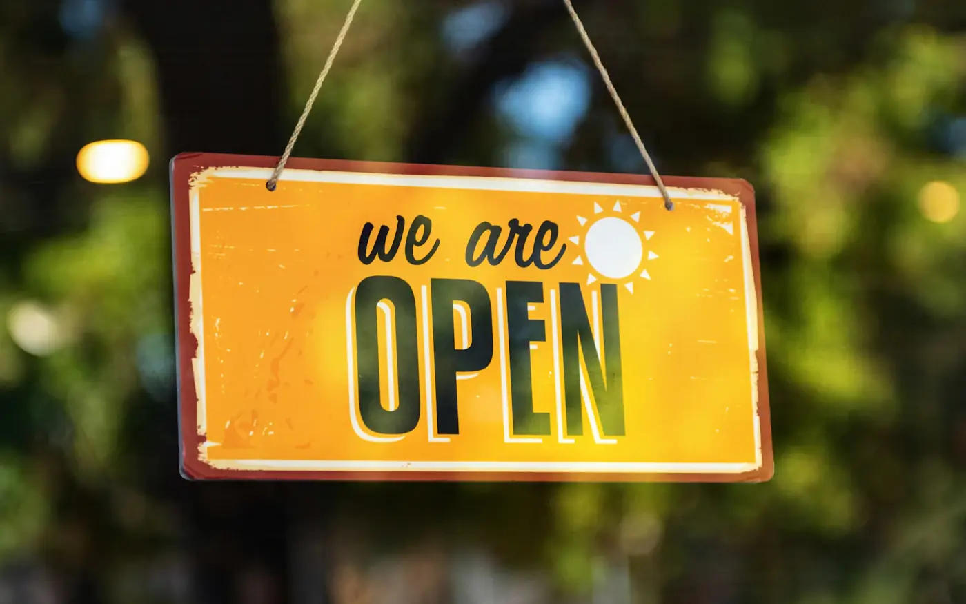A yellow “We are open” sign hanging in a shop window