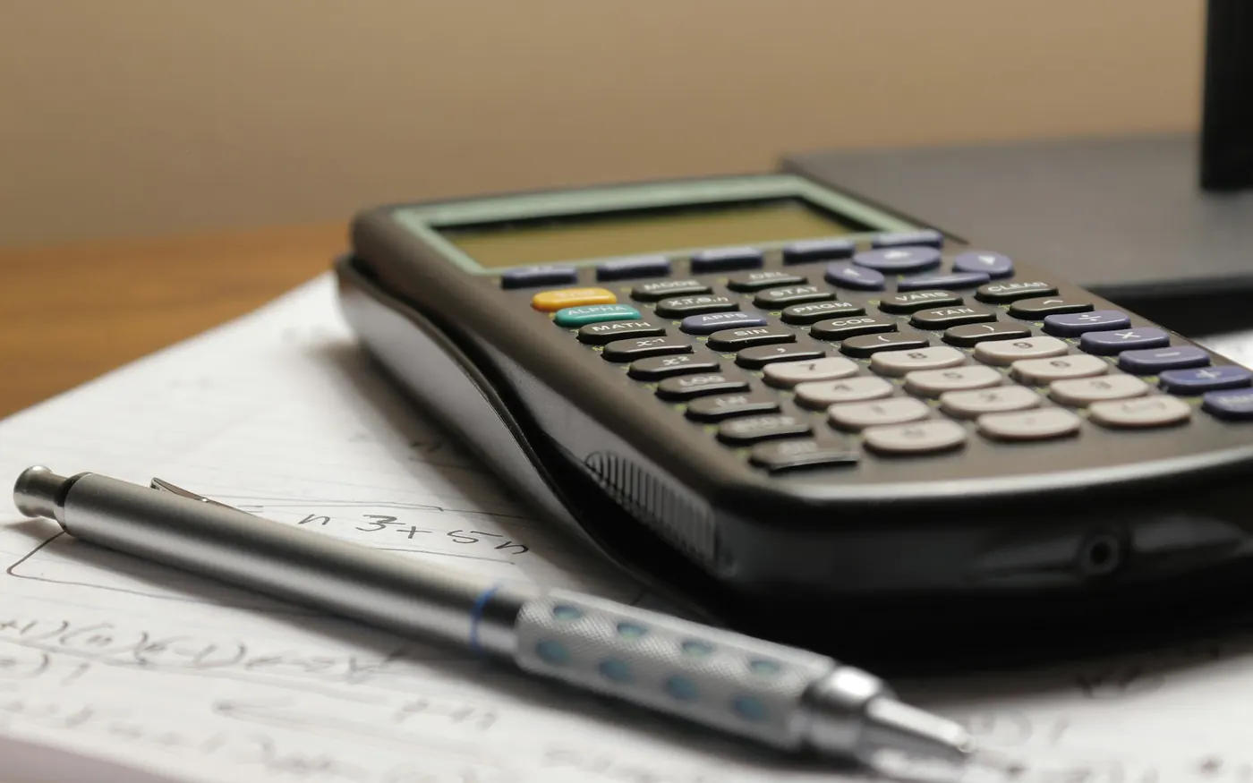 A calculator and a pen resting on a sheet of paper with figures