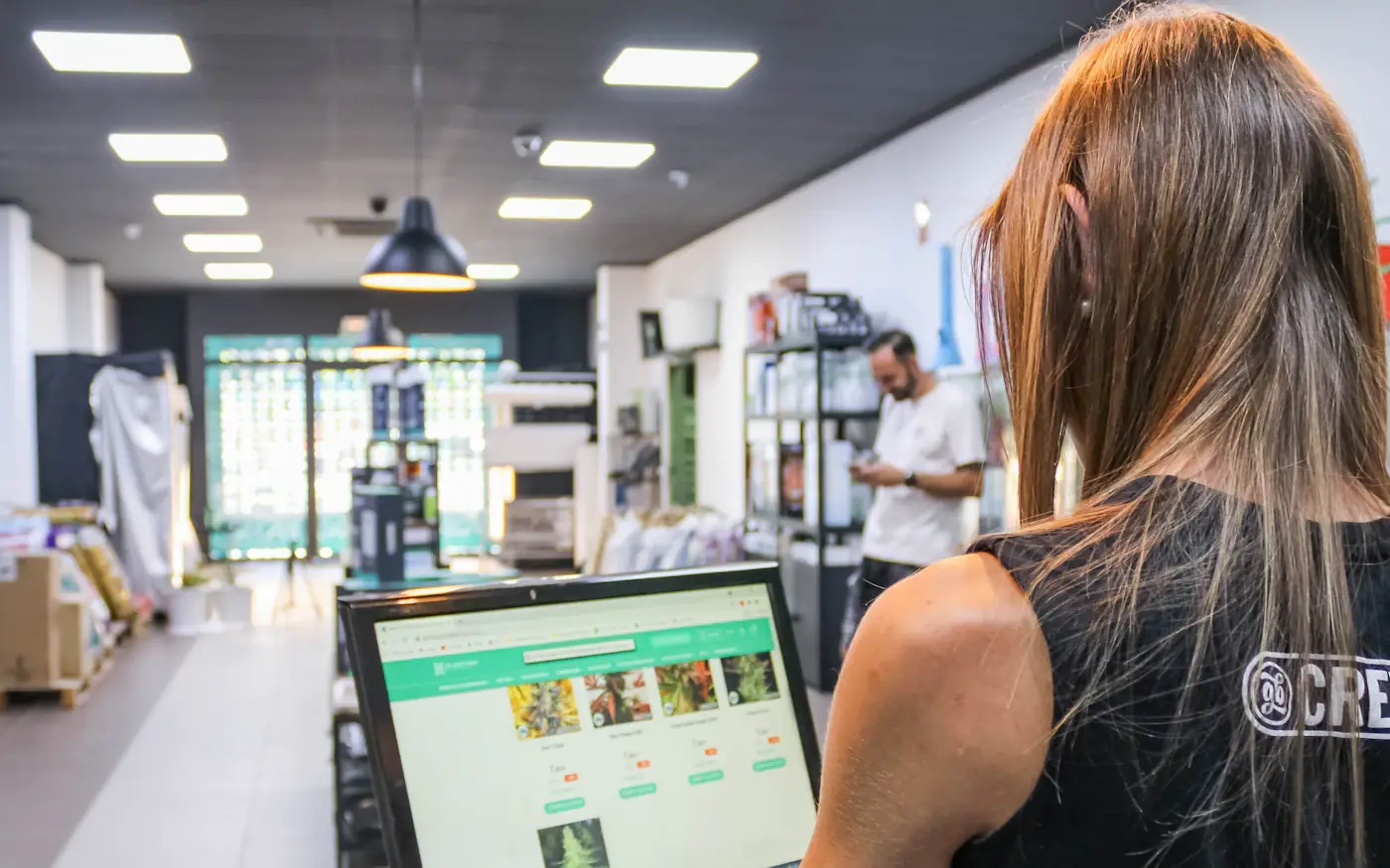 A shop worker at a computer on the counter, with the shop floor behind her